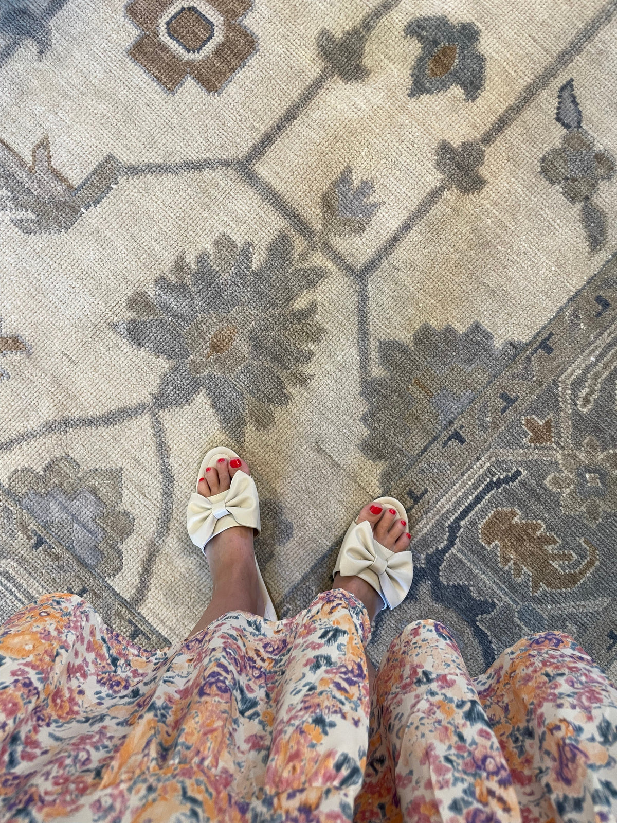 A view of a person's feet wearing floral patterned shoes, standing on a traditional style multicolored area rug with a floral pattern.
